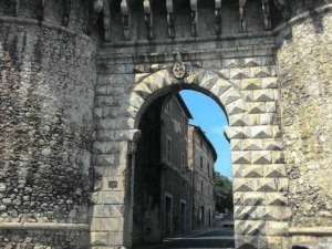 Antica porta in pietra e mattoni, ingresso storico in un pittoresco borgo italiano, con edifici tradizionali e cielo azzurro sullo sfondo.