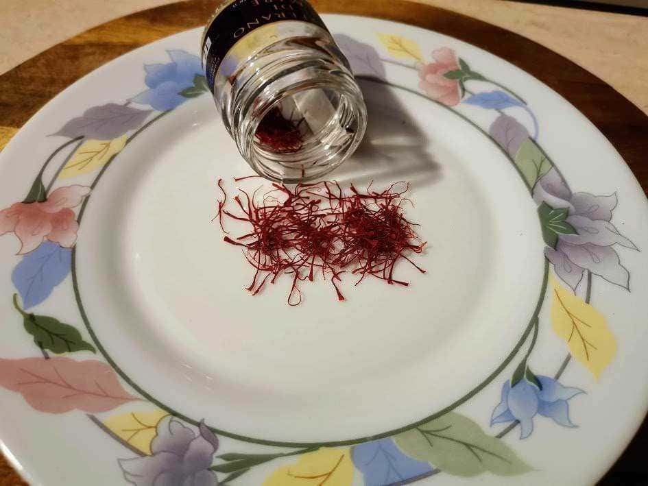 Fiocchi di zafferano con contenitore di spezie su piatto decorativo, ingrediente essenziale per cucina gourmet, perfetto per ricette tradizionali e sofisticate.