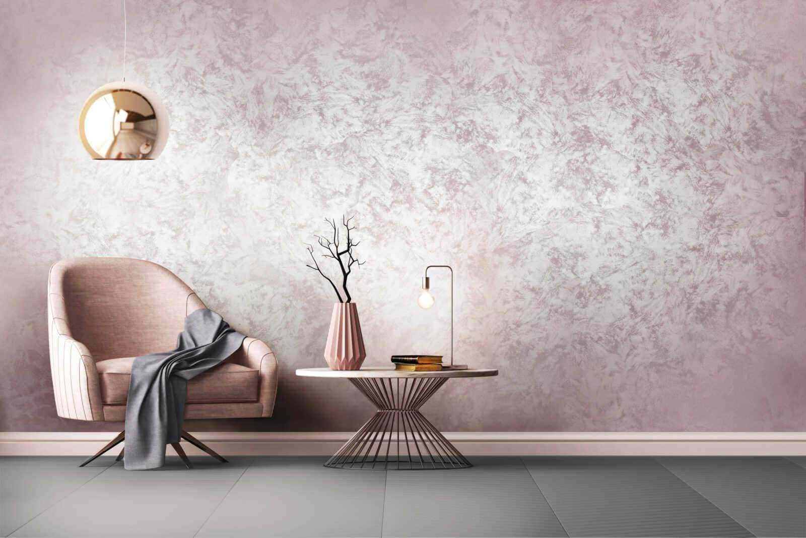 Elegante zona living con poltrona rosa, tavolino decorativo con lampada e vaso con ramo secco, parete rosa con texture sofisticata, design moderno e raffinato, ideale per arredo interno di stile contemporaneo.