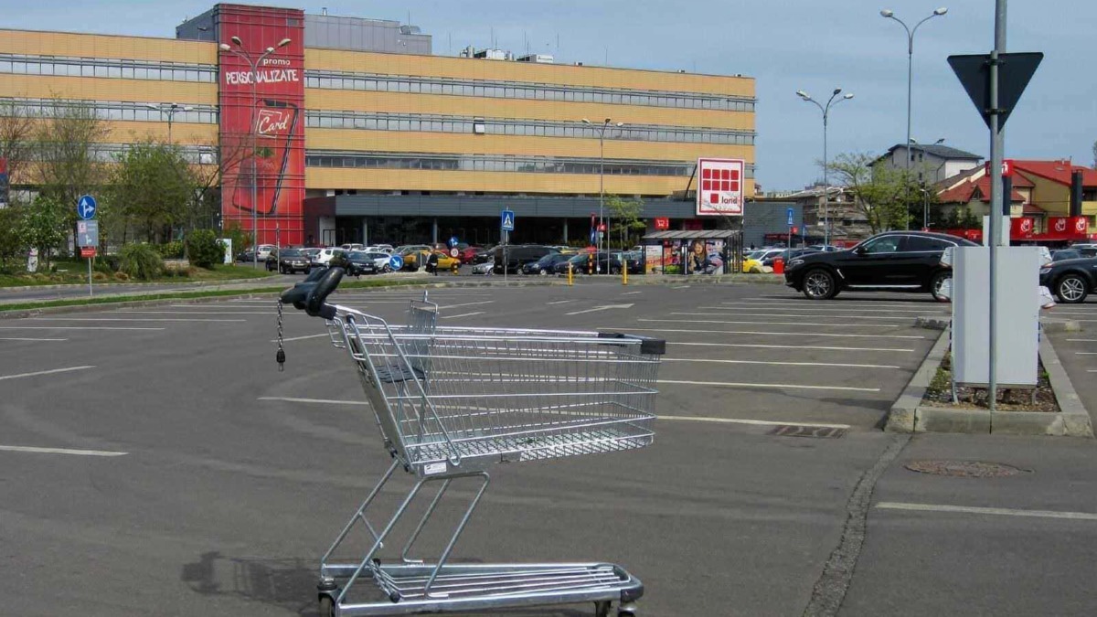 Carrello della spesa in un parcheggio di supermercato con edificio commerciale in background.