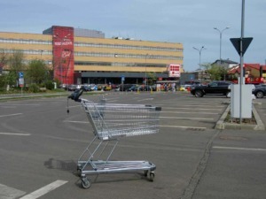 Carrello della spesa in un parcheggio di supermercato con edificio commerciale in background.