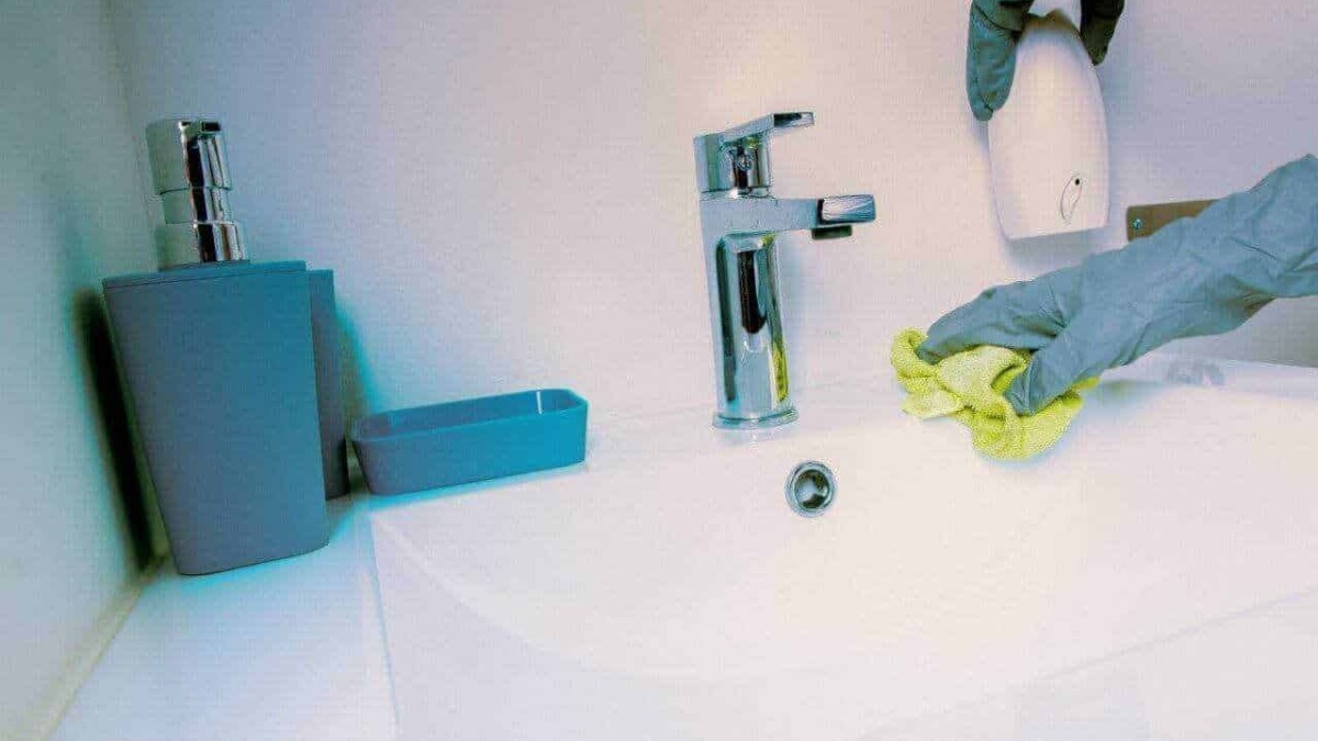 Pulitore che igienizza il lavandino con guanti di gomma e panni, attenzione all'igiene domestica, pulizia e sanificazione ambientale, focus sulla cura della casa e sanificazione.