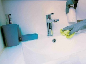 Pulitore che igienizza il lavandino con guanti di gomma e panni, attenzione all'igiene domestica, pulizia e sanificazione ambientale, focus sulla cura della casa e sanificazione.