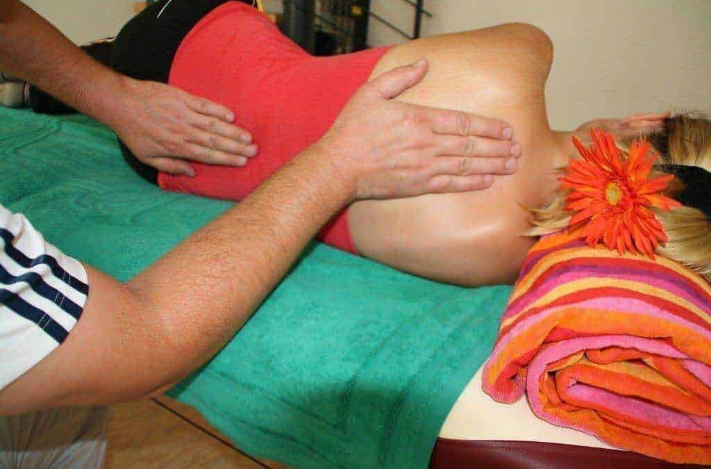 Massaggiatore che esegue un massaggio sulla schiena di una donna sdraiata su un lettino da spa con asciugamano colorato e fiori, trattamento rilassante e terapeutico.