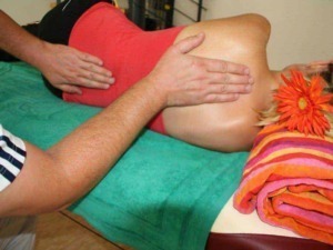 Massaggiatore che esegue un massaggio sulla schiena di una donna sdraiata su un lettino da spa con asciugamano colorato e fiori, trattamento rilassante e terapeutico.