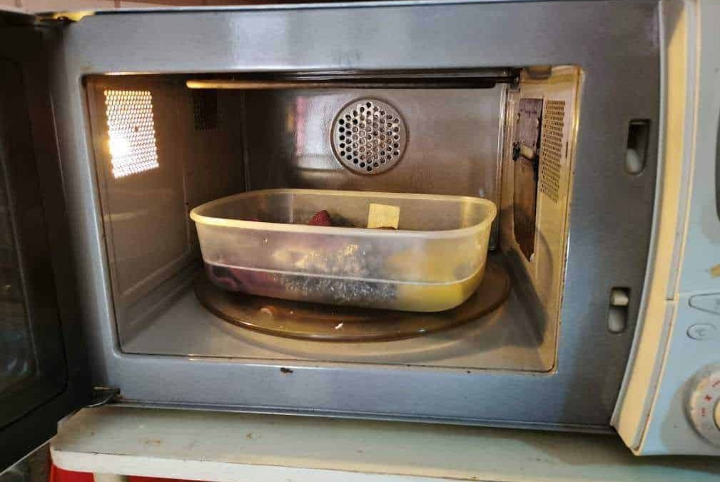 Microonde con contenitore di plastica all'interno, cucina domestica, utilizzo del microonde, riscaldamento alimenti, elettrodomestici da cucina.