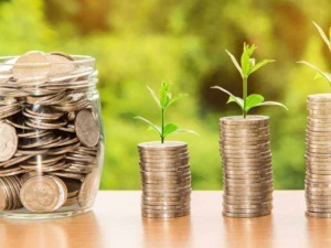 Fondo: Monete di euro impilate con piante che crescono da ognuna, simbolo di crescita finanziaria e investimenti. Ricchezza, risparmio e crescita economica rappresentati visivamente.