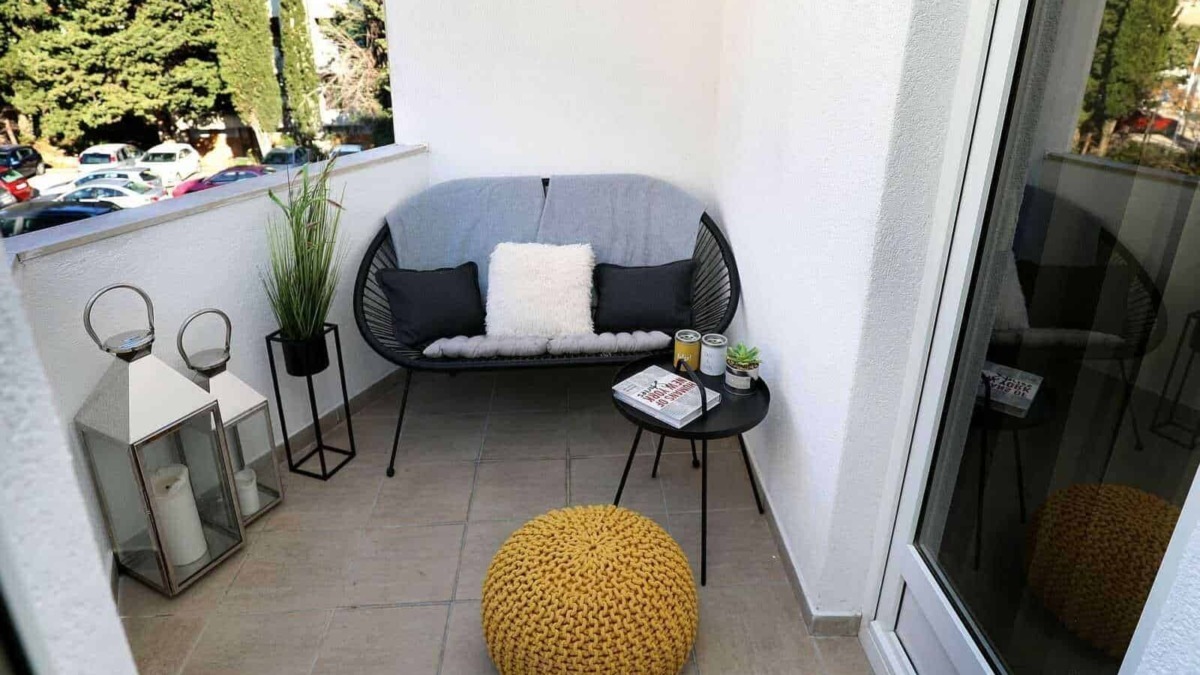 Accogliente balcone con seduta moderna e cummerse di cuscini neri e bianca, arredi eleganti con piante e candela, ideale per relax e momenti di relax all'aperto.