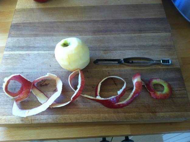 Mela verde e bucce di mela affettate disposte su un tagliere di legno con un pelaverdure, un utensile per pelare e una mela intera pronta per essere sbucciata.
