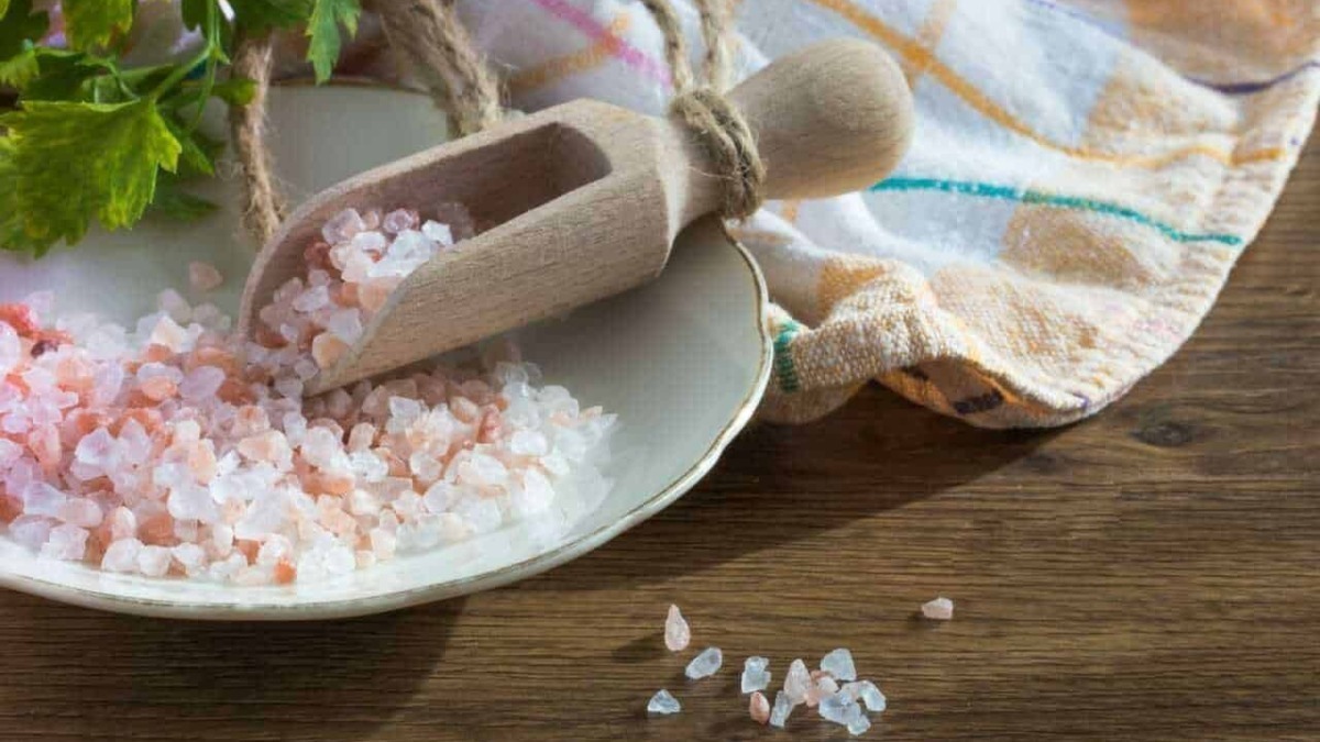 Sale rosa grosso per cucina integrata in sale naturale, ideale per arricchire piatti e alimenti, con cucchiaio di legno su piatto di ceramica, sul tavolo di legno.