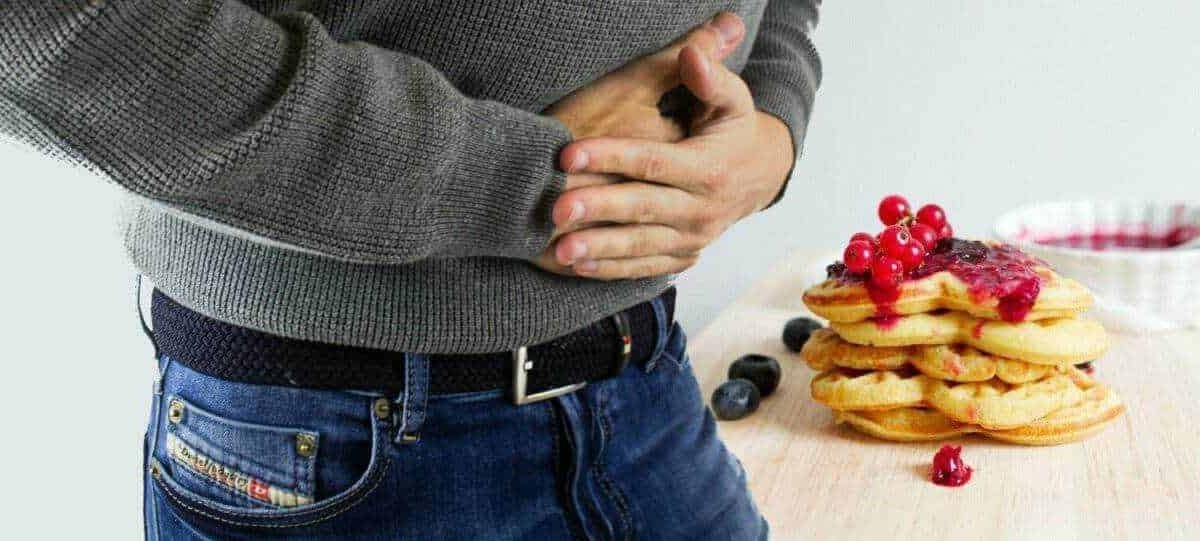 Mal di stomaco da cibo o digestione, persona dolorante con stomaco che si stringe, pancake con marmellata e frutti di bosco, problema digestivo.