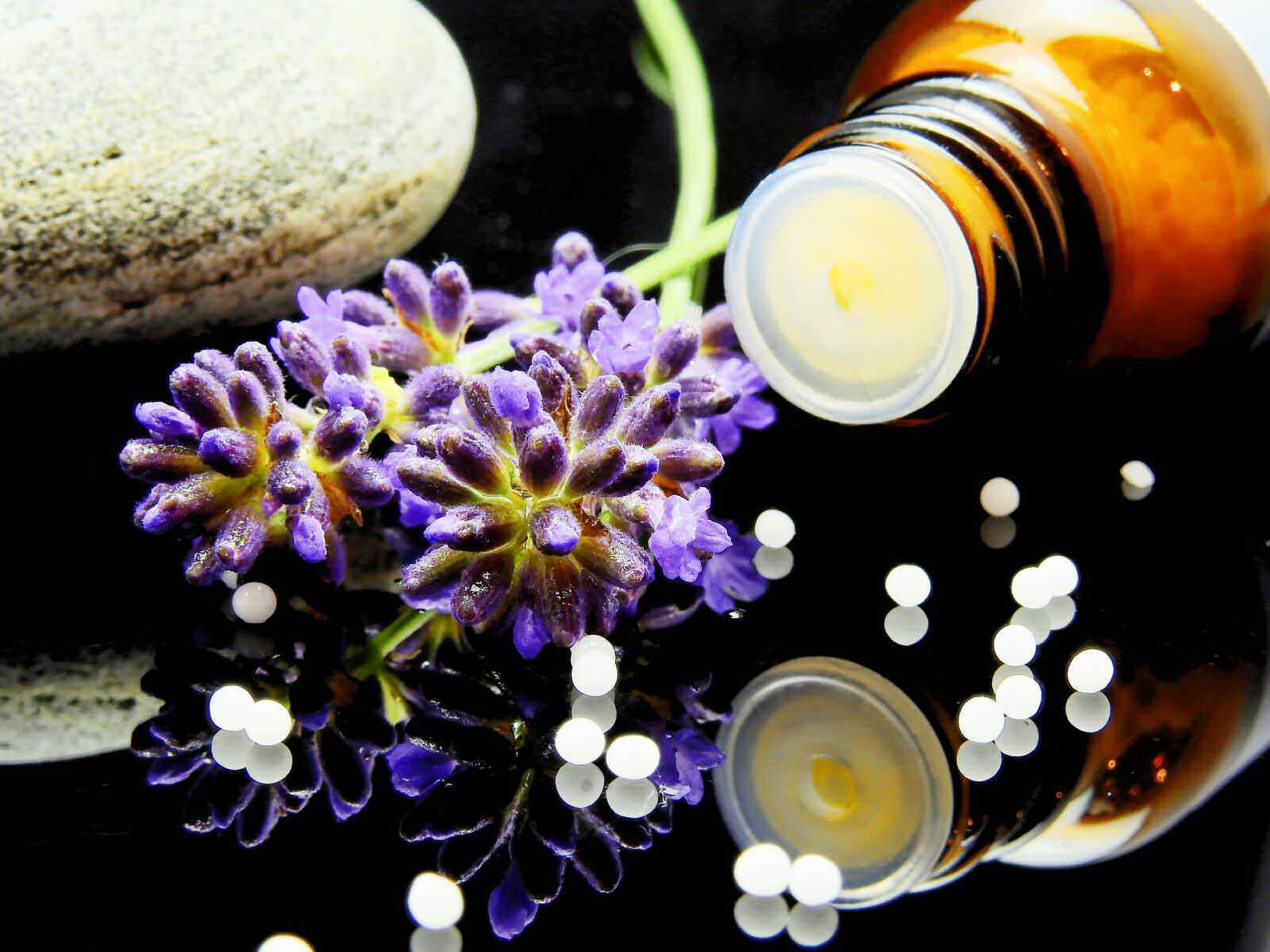 Aromaterapia con olio essenziale di lavanda, pietra levigata e pillole di medicina naturale su sfondo nero.