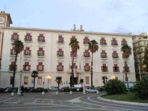 Appunti Sul Blog building con facciata storica e palme, centro città Sicilia, architettura urbana e turismo locale, immagini di carattere storico e culturale.