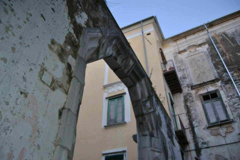 Relitto di un vecchio arco in pietra su un edificio storico abbandonato, con muri consumati e finestre con vetri rotti, scenario di deterioramento e decadenza urbana.