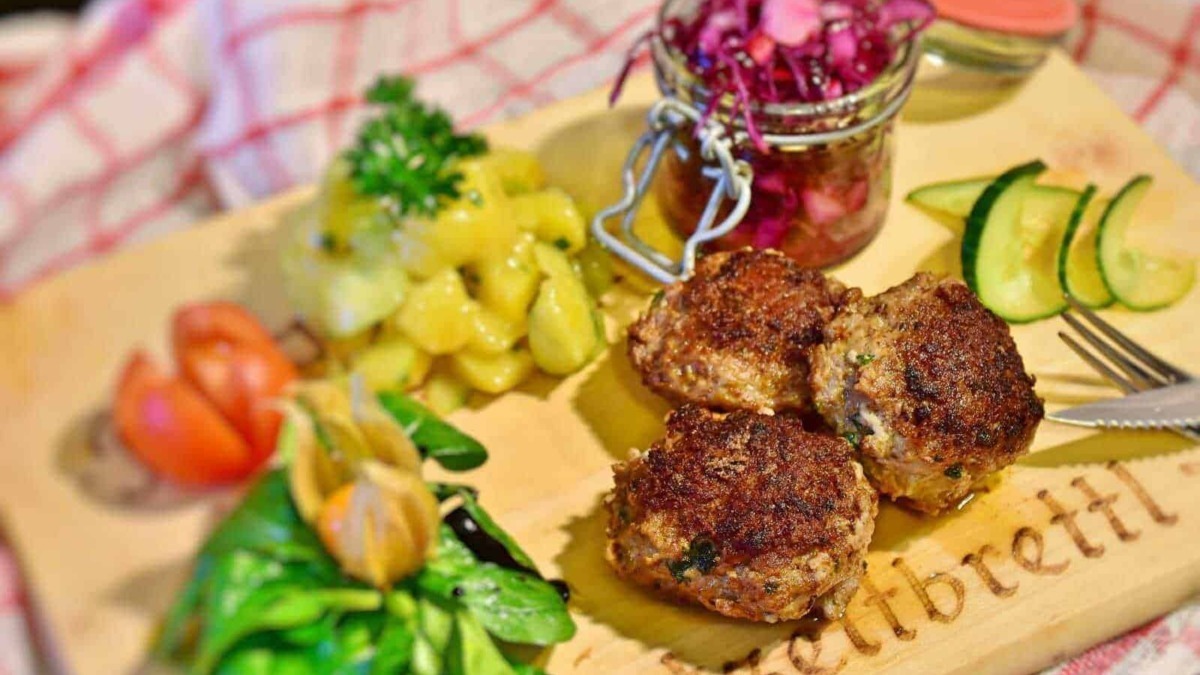 Fagottini di carne ripieni di formaggio e spezie, serviti con contorni di insalata, cetrioli, pomodorini e insalata di cavolo rosso, presentati su un tagliere di legno in stile rustico.