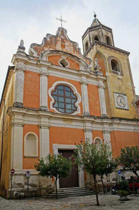 Campanile e facciata della chiesa barocca di origine italiana, dipinta in tonalità calde di arancione e giallo, con dettagli architettonici decorativi e finestre ornate, situata in un centro storico di una città italiana.