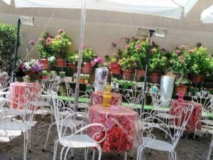 Balcone con tavoli in ferro battuto e fiori colorati, spazio esterno per relax e socializzazione in un ambiente estivo e accogliente.