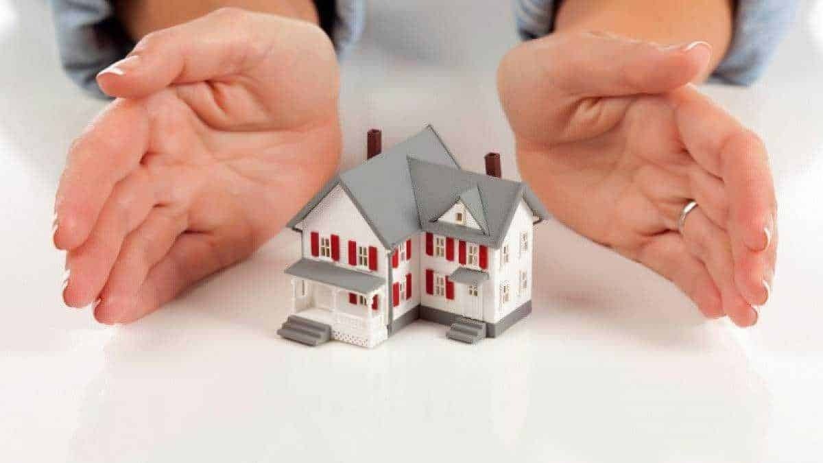 Protezione della casa e sicurezza domestica, mani che proteggono un modellino di casa, immagine concettuale di tutela e sicurezza abitativa.
