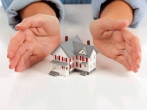 Protezione della casa e sicurezza domestica, mani che proteggono un modellino di casa, immagine concettuale di tutela e sicurezza abitativa.