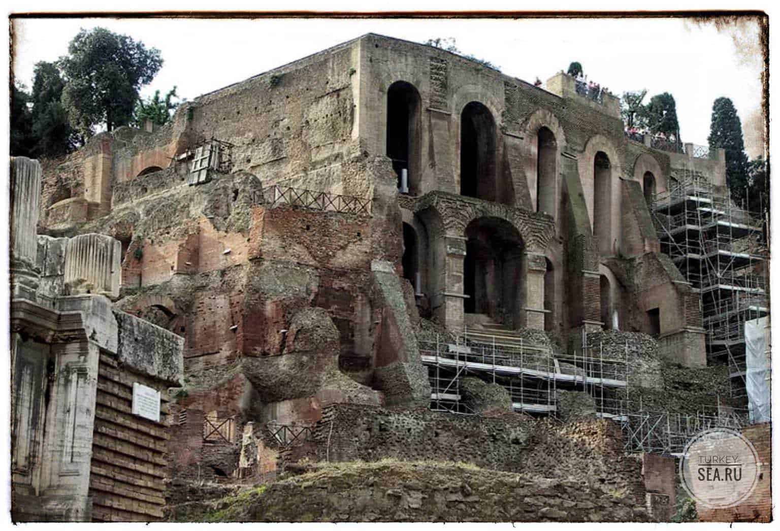 Come vivevano i Romani la vita quotidiana 3 Antica rovina archeologica con resti di un edificio storico, probabilmente parte di un sito romano o antico, con scale di accesso e scavi archeologici, circondata da vegetazione e scaffalature di restauro.