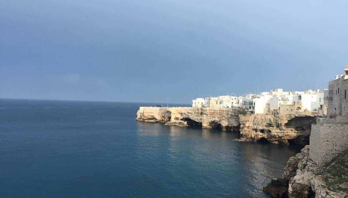 Pensilina sulla scogliera con case bianche sul mare, viste dal mare, coste di roccia e acque turchesi, paesaggio costiero mediterraneo, promotes Italy travel, turismo costiero e bellezze naturali.