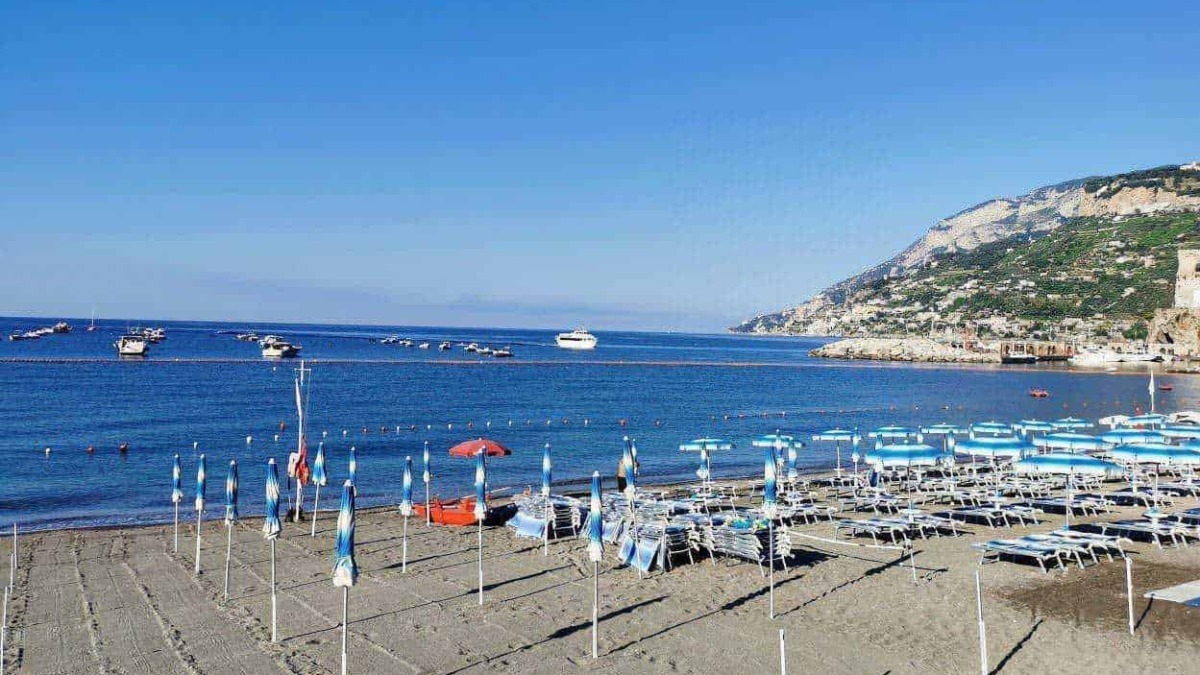 Spiaggia di Capri con ombrelloni e sdraio al mare, vista panoramica sulla baia e le colline circostanti. Perfetta per relax e vacanze estive in Italia, con acque cristalline e paesaggi mozzafiato.