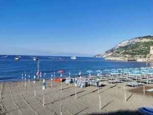 Spiaggia di Capri con ombrelloni e sdraio al mare, vista panoramica sulla baia e le colline circostanti. Perfetta per relax e vacanze estive in Italia, con acque cristalline e paesaggi mozzafiato.