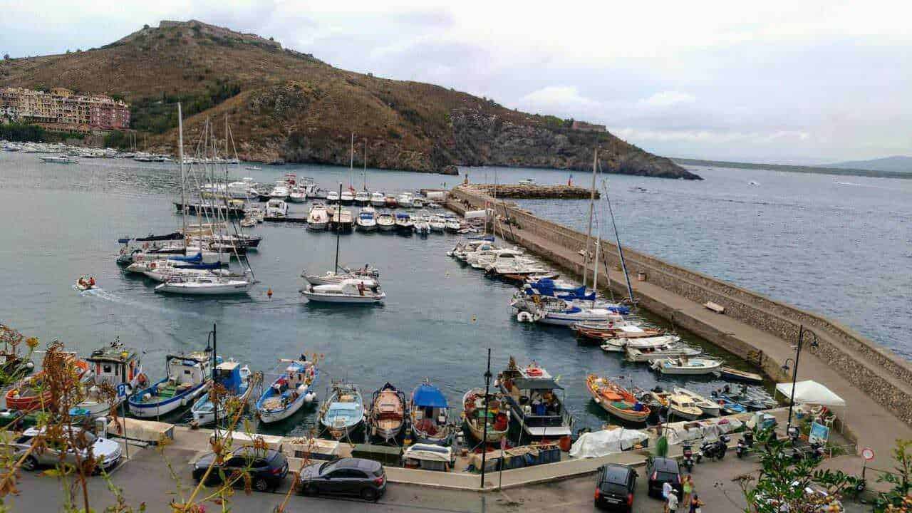 Barca, porto turistico e paesaggio costiero in Italia, con vista sul mare, imbarcazioni, promontorio e cielo nuvoloso, perfetto per articoli di blog su destinazioni di viaggio.