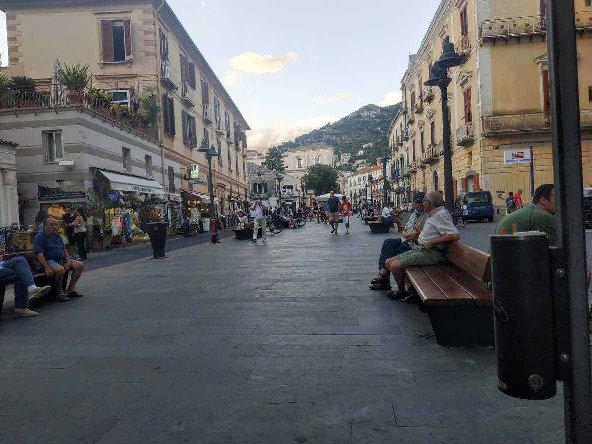 Vivace strada pedonale nel centro storico con negozi, bar e persone che si rilassano, circondata da edificio storici e affascinanti vicoli, con vista sulle colline circostanti