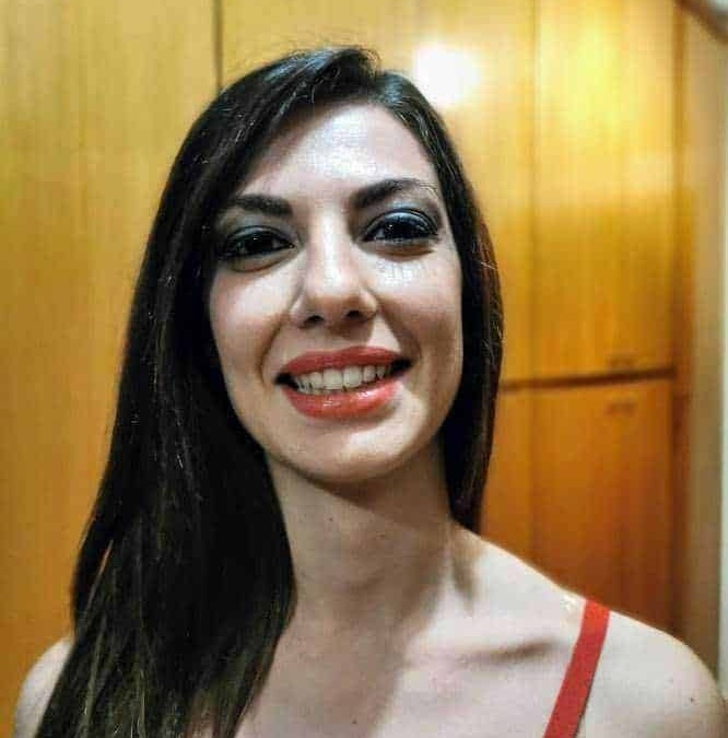 Bellissima donna sorridente con trucco intenso e capelli lunghi, sfondo di mobili in legno, ideale per articoli su bellezza, stile e lifestyle femminile.