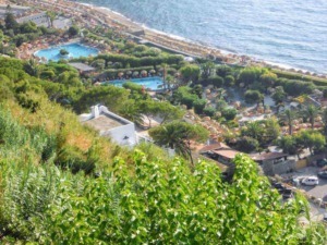 Spiaggia affacciata sul mare con piscine e vegetazione rigogliosa, vista dall'alto di una località turistica al mare in Italia.