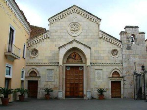 Facciata della chiesa storica con archi e dettagli in pietra, situata in un'area urbana con piante in vaso ai lati dell'ingresso.