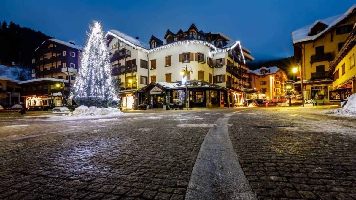 Luminoso paesino alpino decorato con luci natalizie e alberi di Natale, atmosfera festiva invernale con edifici tradizionali e strade ciottolate.