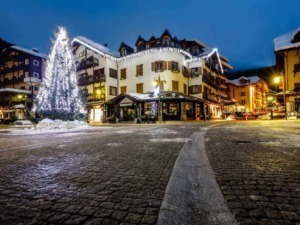Luminoso paesino alpino decorato con luci natalizie e alberi di Natale, atmosfera festiva invernale con edifici tradizionali e strade ciottolate.