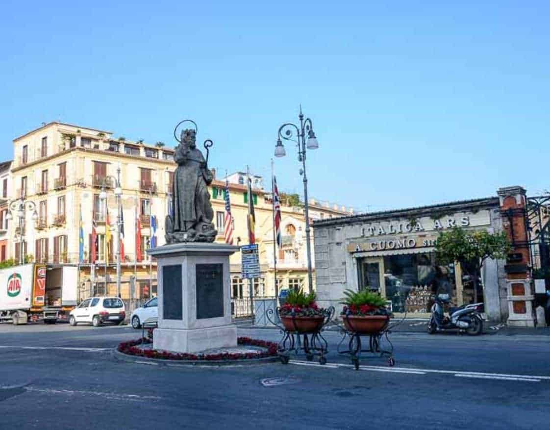 Statua di un santo in centro a Napoli, Italia, con negozi e auto sullo sfondo, simbolo di arte e cultura italiana.
