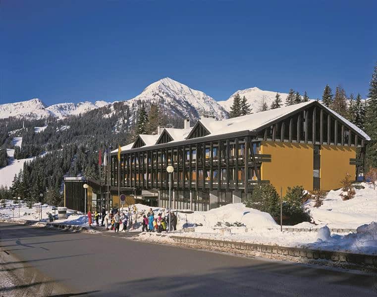 Dormire in un Hotel a Madonna di Campiglio tra neve perenne e laghi azzurri 8 Hotel moderno immerso nella neve con montagne e laghi azzurri sullo sfondo, ideale per soggiorni invernali e relax tra natura e paesaggi mozzafiato.
