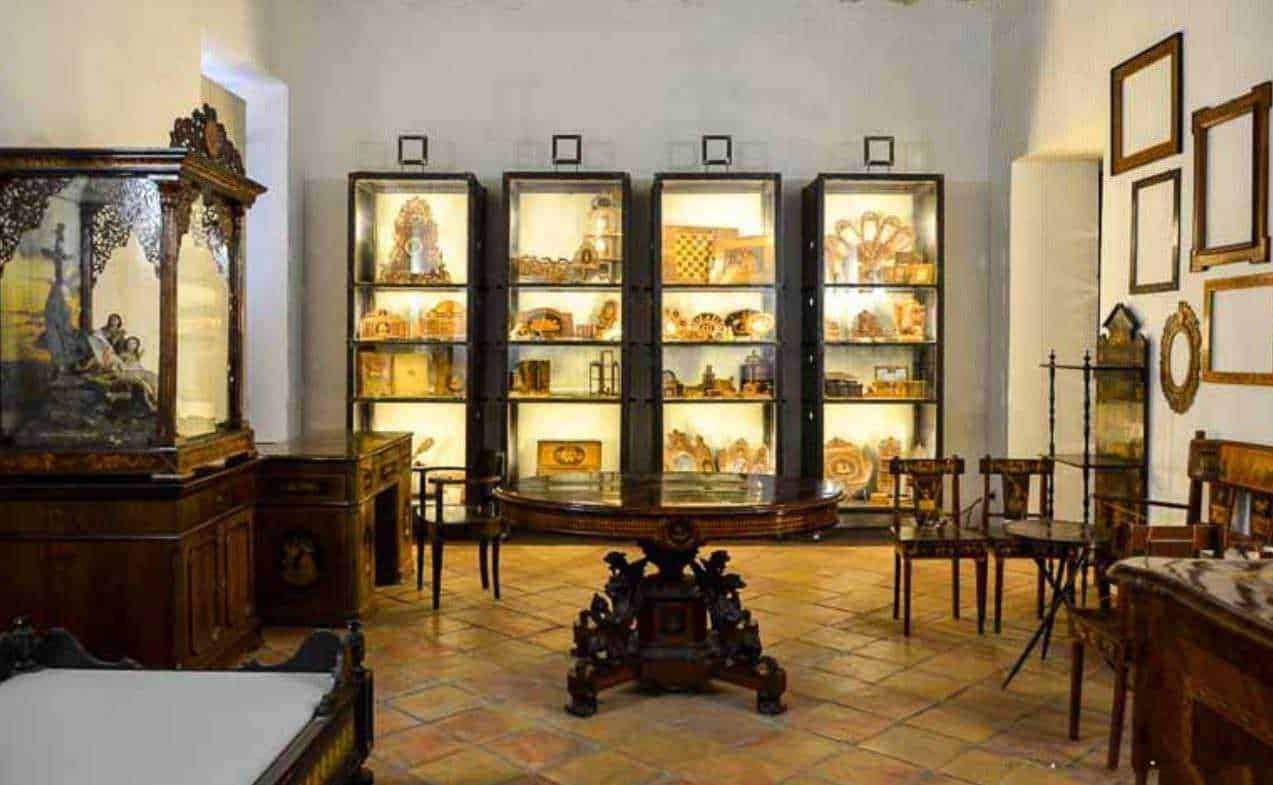 Vetrine di oggetti d'antiquariato in una stanza di museo con mobili in legno e pareti decorate.