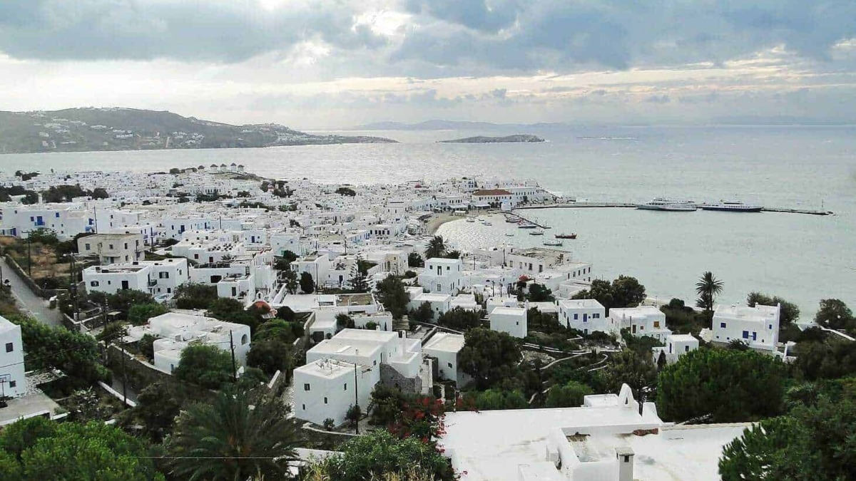 Pointer osteria di Mykonos, Grecia, vista panoramica delle case bianche, edificio in stile tradizionale, mare cristallino, cielo nuvoloso, attività turistica, località costiera.