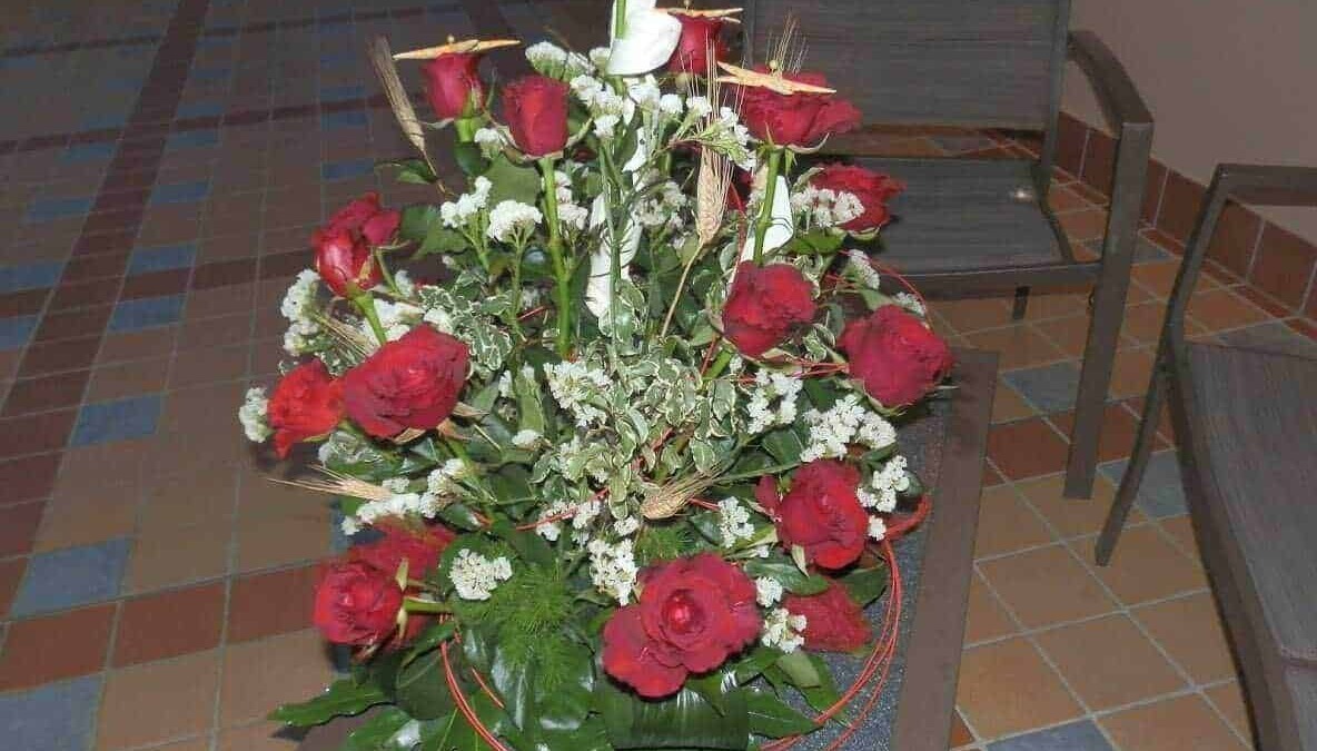 Vaso con fiori natalizi, tra cui piante di agrifoglio con foglie verdi lucide e boccioli rossi intensi, decorato con nastri rossi e foglie di felce.