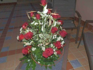 Vaso con fiori natalizi, tra cui piante di agrifoglio con foglie verdi lucide e boccioli rossi intensi, decorato con nastri rossi e foglie di felce.