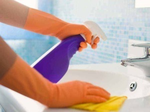Pulizia e igiene del bagno, donna con guanti arancioni che utilizza spray disinfettante e spugna per pulire il lavabo e il rubinetto.