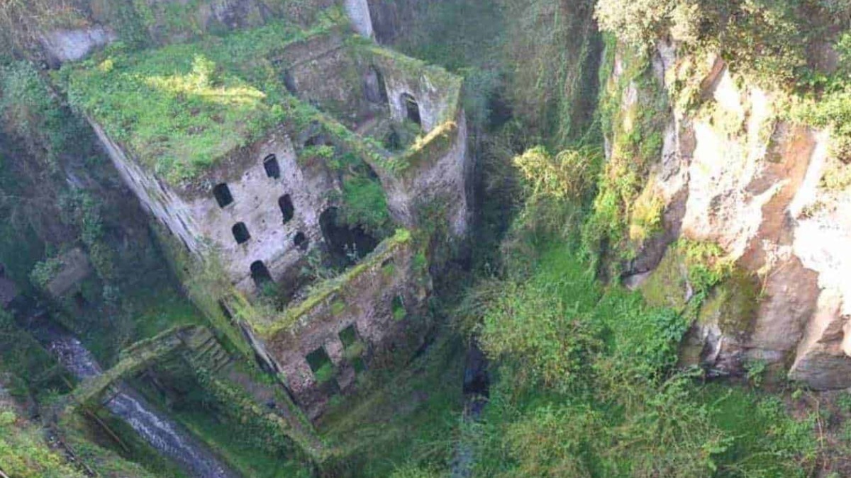 Antico edificio abbandonato ricoperto di vegetazione in una gola naturale, immerso in un paesaggio selvaggio e misterioso.