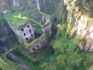 Antico edificio abbandonato ricoperto di vegetazione in una gola naturale, immerso in un paesaggio selvaggio e misterioso.