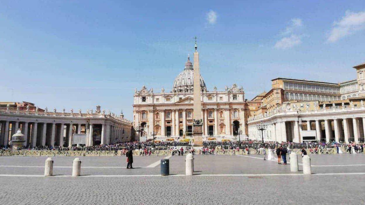 Città del Vaticano, Piazza San Pietro con la basilica e obelisco al centro, affollata di visitatori e turisti, cielo sereno, esempio di arte e architettura religiosa.
