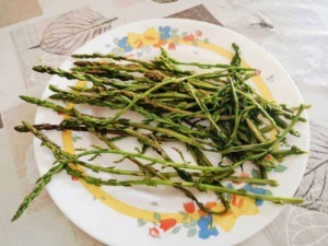 Asparagi freschi su piatto decorato con motivi floreali, simbolo di cucina sana e alimentazione naturale.