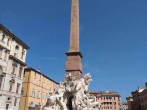Colonna dell'Obelisco e fontana in Piazza Navona, Roma, Italia, con sculture barocche e edificio storico sullo sfondo.