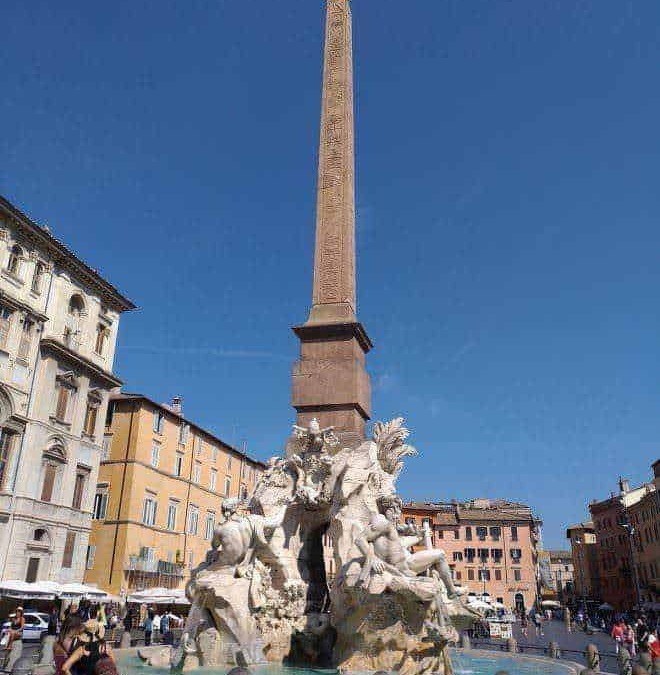 Colonna dell'Obelisco e fontana in Piazza Navona, Roma, Italia, con sculture barocche e edificio storico sullo sfondo.