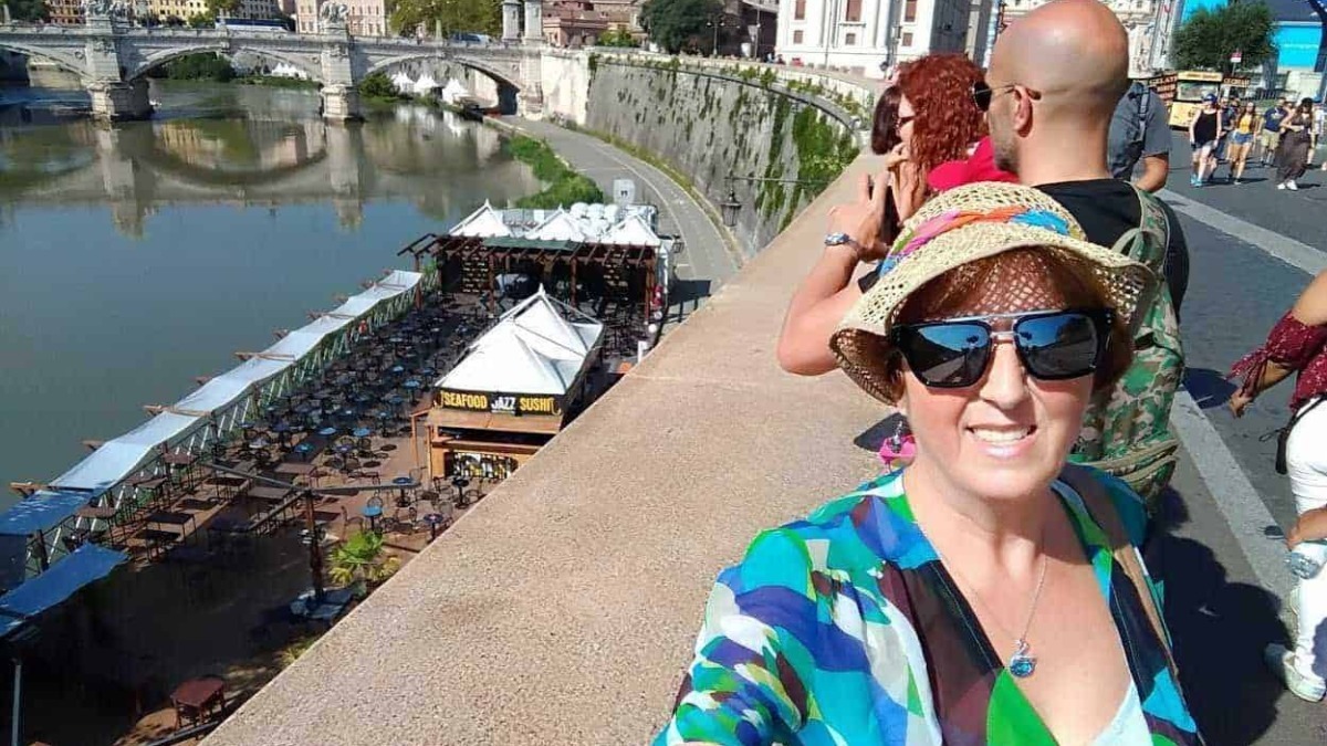 Passeggeri che ammirano il fiume Tiber con un ponte storico a Roma, con vista sulla Basilica di San Pietro, in una giornata di sole.