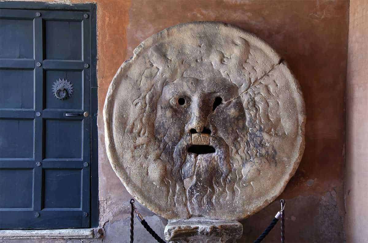 Antico monumento romano con testa di Medusa in pietra, decorazione storica su parete in mattoni rossi, adiacente a porta in legno blu, atmosfera storica e artistica.