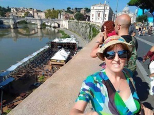Passeggeri che ammirano il fiume Tiber con un ponte storico a Roma, con vista sulla Basilica di San Pietro, in una giornata di sole.